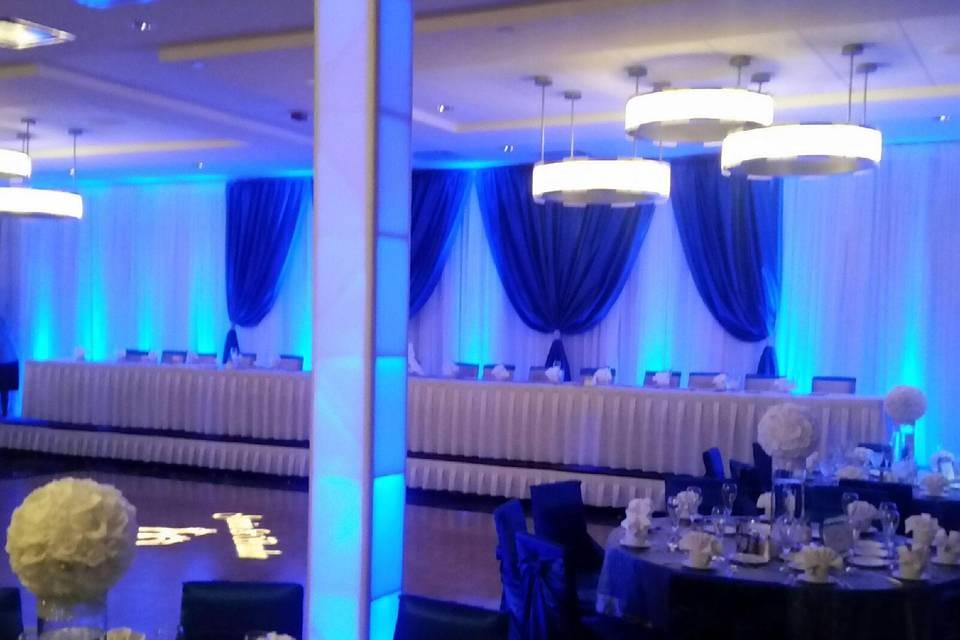 Blue lighting highlights the white sheer drapes with royal blue satin drapes and white towers surrounding the dance floor.