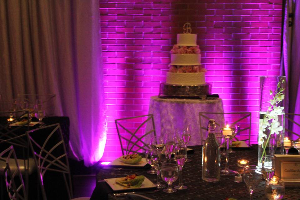 Pink / Purple lighting on a brick wall combines with the silver and white drape and linens to brings romance and softness a contemporary/ industrial space.