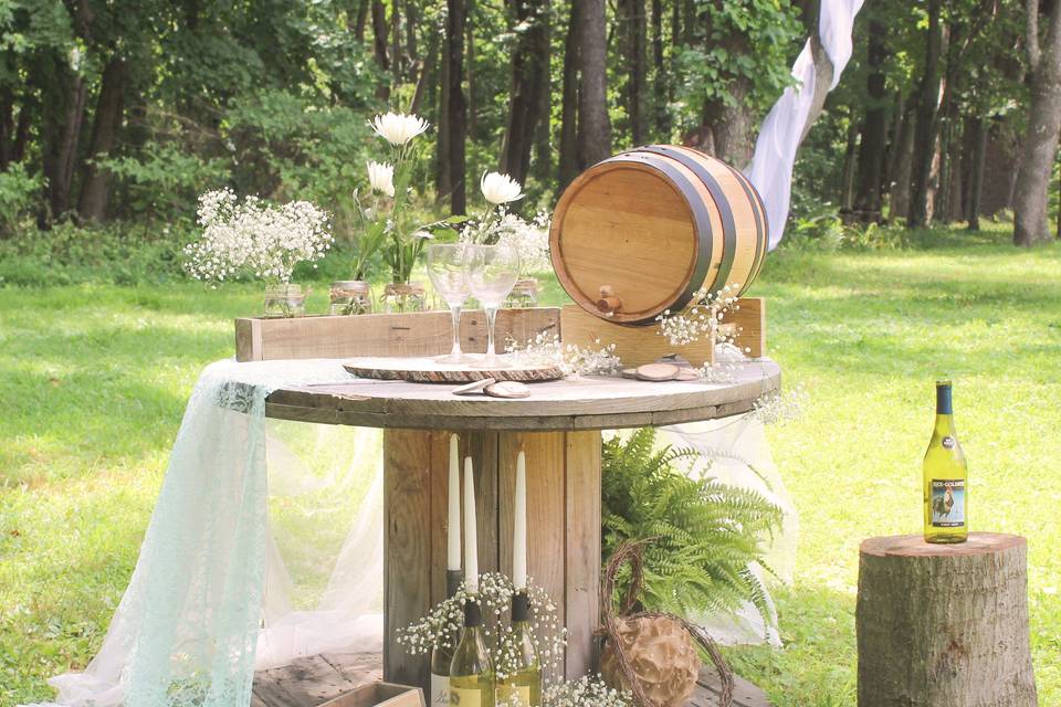 Greet your guests with an inviting table, featured is a miniature wine barrel converted into a gift card box, delicate lace linens, flowers in mason jars placed in a re-purposed rustic wood box and a glass of wine to start the evening.