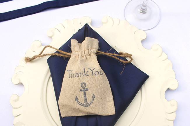 Place setting with charger plate, navy napkin and a nautical thank you gift bag.