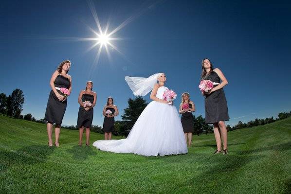 Bride surrounded by bridesmaids in grass.