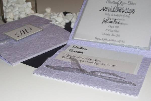 High School Crush
This invitation has truly been a favorite amongst our clients. This unusual pocket fold is made with a lilac handmade paper that is crushed, crinkled and coated for a shimmer affect. The invitation is printed on a bright white metallic paper and backed with a matching silver metallic paper. A vellum overlay will display a poem, monogram or wording of choice and everything will be attached at the top with a silver brad. The pocket will be created with a silver sheer ribbon and can hold all of the necessary information cards of choice.