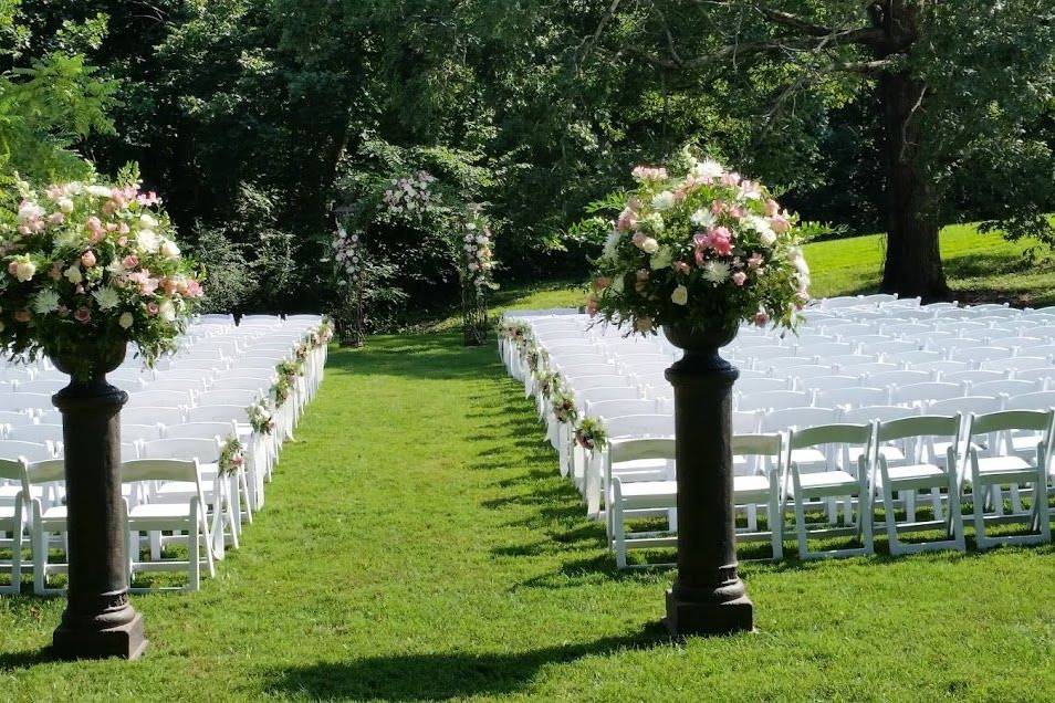 Ceremony setup with floral pillars, arch and white wedding chairs