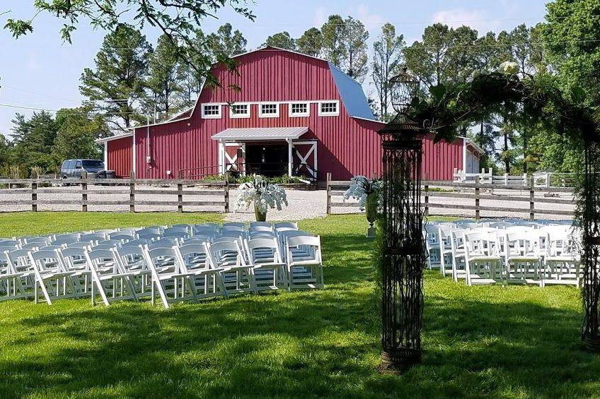 Ceremony with metal arch, orchids in urns and white wedding chairs