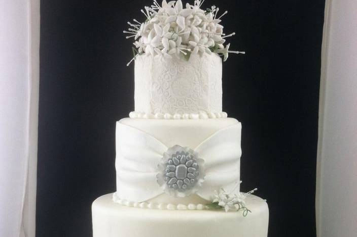 Four tier wedding cake with handmade brooches and stephanotis flowers. Gathered fabric and lace work on all tiers.