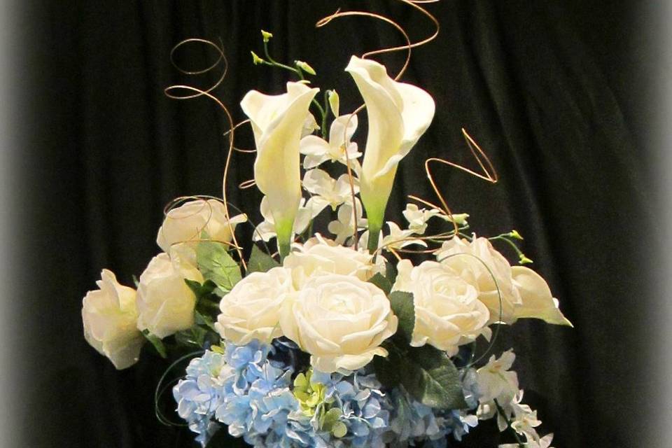 Beautiful centerpiece with Floramatique calla lillies, Real Touch roses, orchids, and blue hydrangea in a clear cylinder vase.