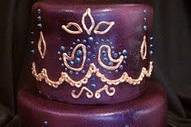 A gorgeous India inspired wedding cake. A backdrop of a deep iridescent purple with hand piped and hand painted details .