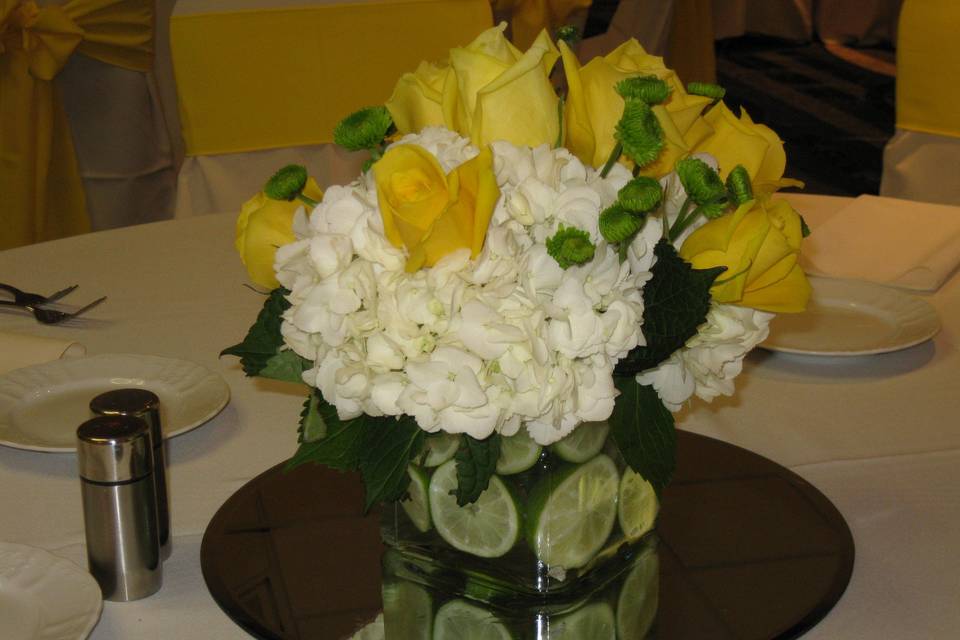 Fun centerpieces with lime filled vases with yellow roses, green button mums and white hydrangea.