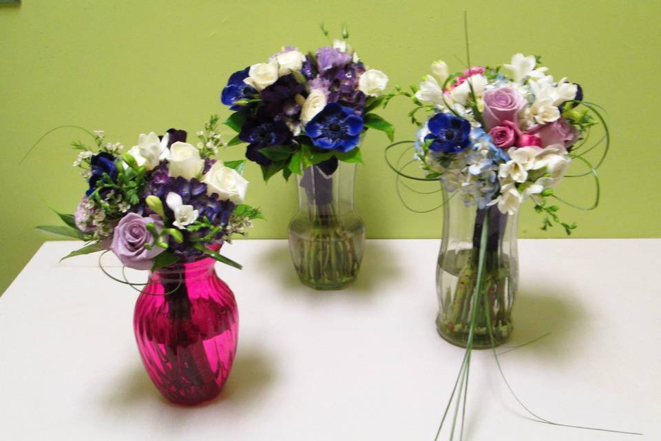 A trio of purple and blue accented bouquets for two brides and their maid of honor.