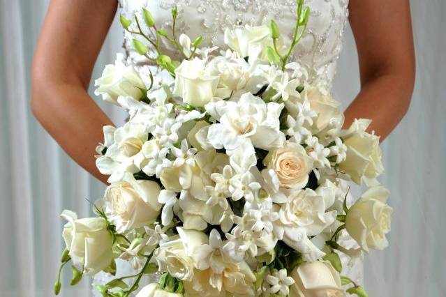 Lavish cascade bridal bouquet featuring all white flowers including roses, gardenias, dendrobium orchids, stephanotis, and accented with sparkling jewels.