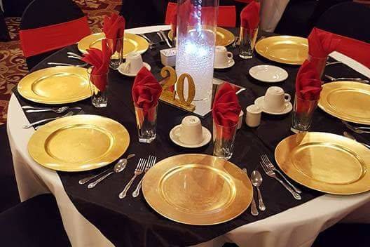 920 Events provided black overlays, gold plate chargers, gold table numbers, tall cylinder vases, black chair covers, red spandex sash bands.
