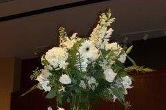 All White flowers arranged in tall vase with curly willow swirled inside the vase.  Dendrobium orchids are cascading down on bullion wire.