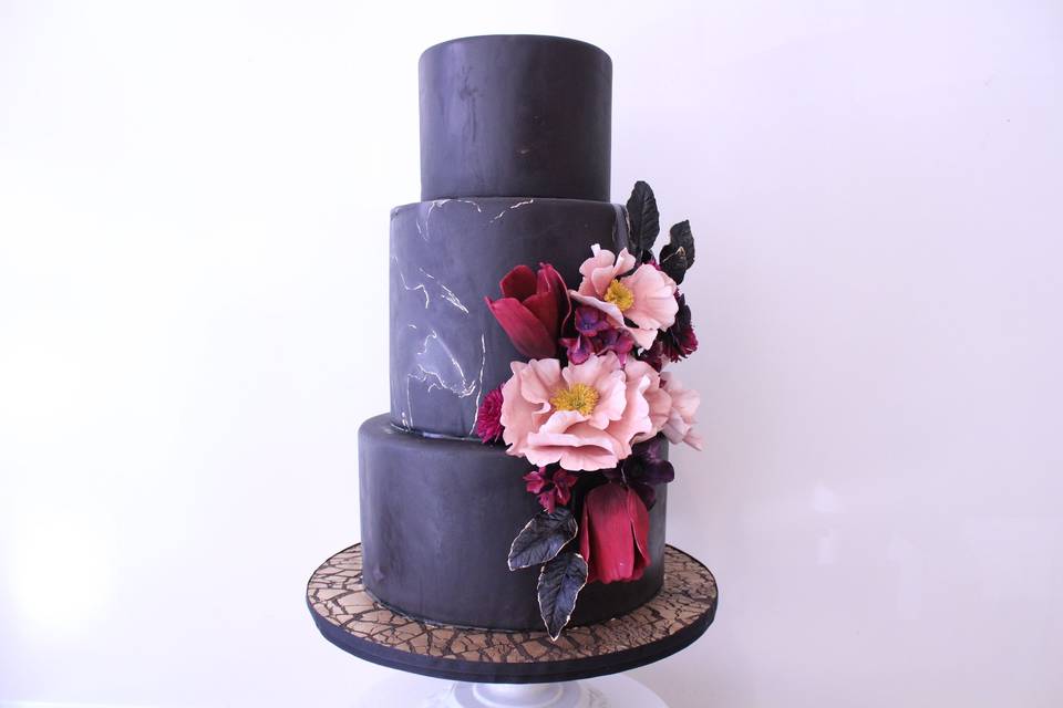 Black marbled tiered cake with sugar flowers and crackle cake board