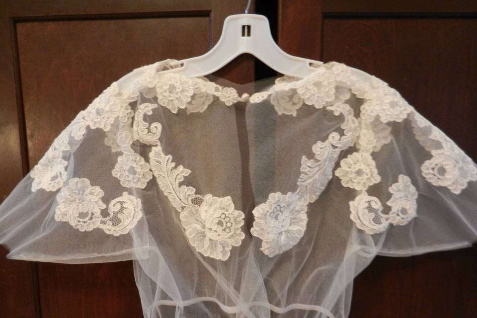 This is the back view of a modesty blouse of appliqued lace on tulle for bride's whose shoulders need to be covered during the ceremony. It has an elasticized bottom and hidden velcro closure.