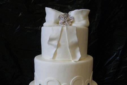 4-tier White Wedding Cake decorated with cirlce designs and bows with edible silver glitter brooches.