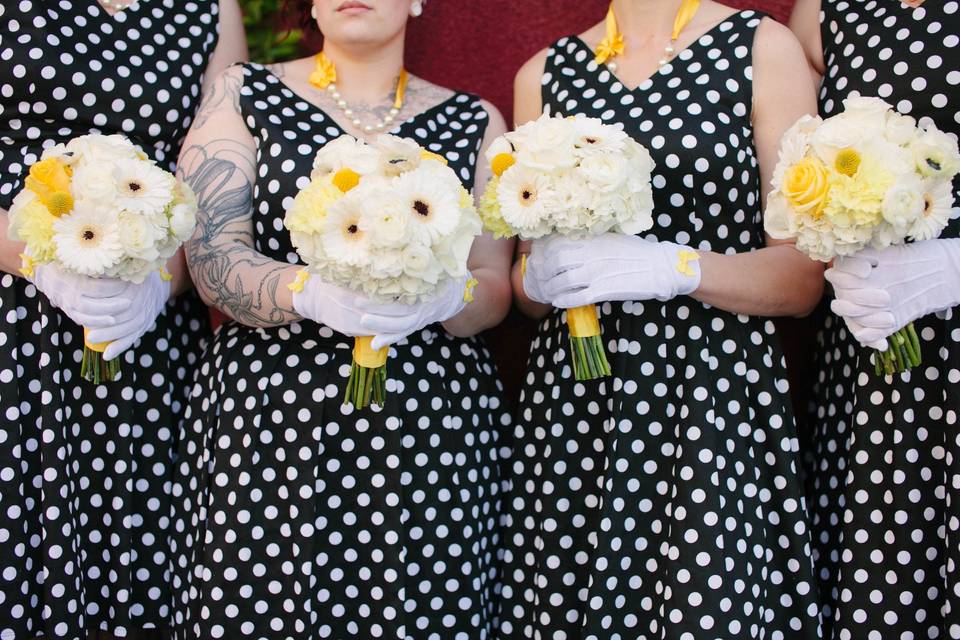 Bridesmaids in polkadots carry bouquets of white with yellow accents.