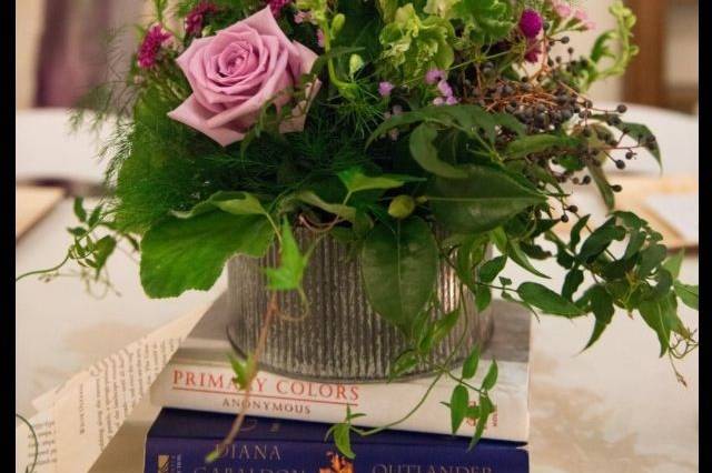 Corrugated tin containers with wild garden style florals atop stacks of books.  Containers available for rent.