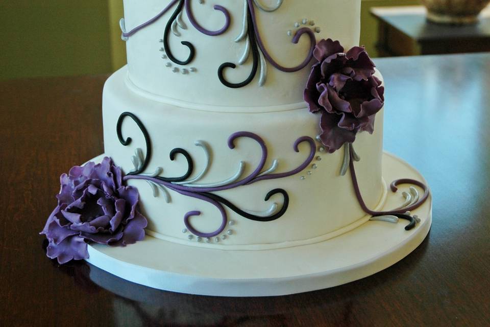 A whimsical but elegant wedding cake, with purple black and silver scrolls and sugar peony flowers.