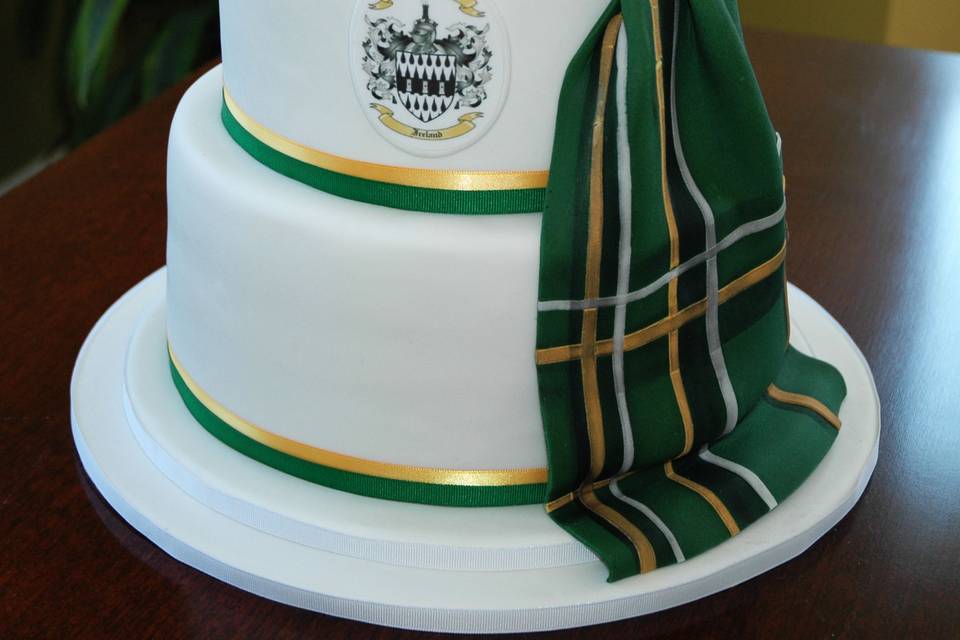 A Scottish themed wedding cake, with fondant kilt as the one worn by the groom.  Coat of arms and gold sugar flower embellishments.