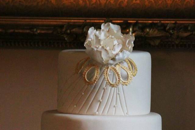 A Gatsby - esque wedding cake, white and gold, with reverse ruffles and a single sugar flower edged with gold color, and accented with pearls.