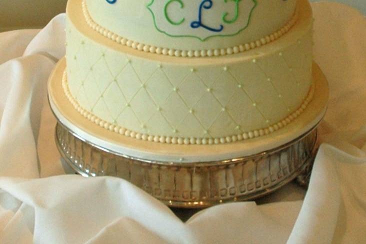 A buttercream finish wedding cake, with quilting, scrolls and a monogram plaque.  Fresh flower topper.