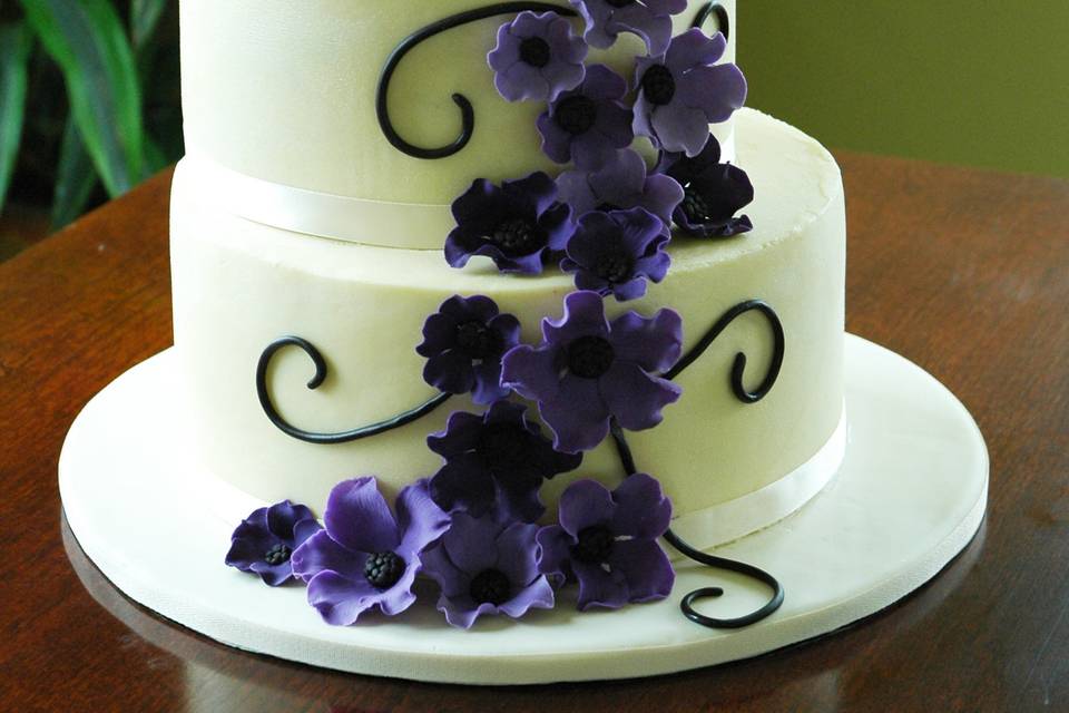 a buttercream wedding cake, in a left stacked configuration, with shades of purple flowers in a cascading pattern.