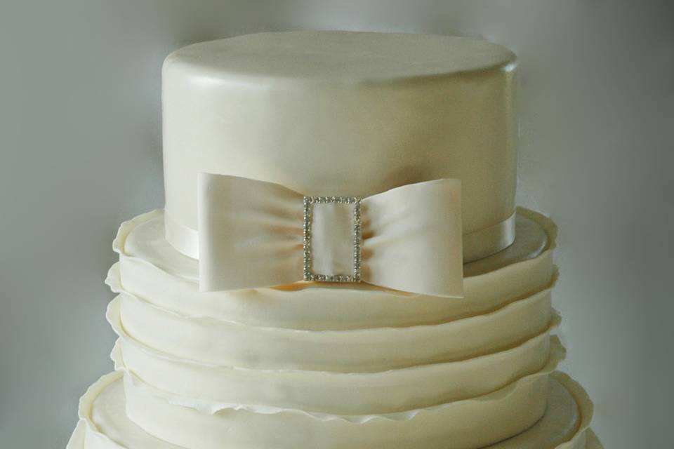 An ivory reverse ruffle formal wedding cake, with bow and rhinestone slider.