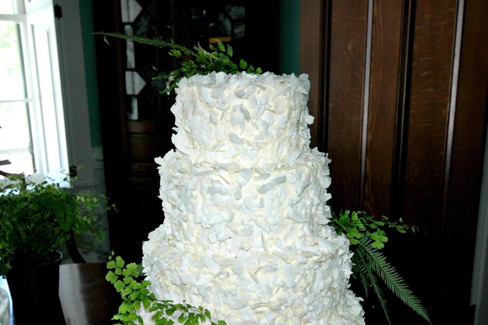 Coconut Lover's flavor wedding cake.  Large coconut shavings around entire cake, and adorned with fresh ferns.