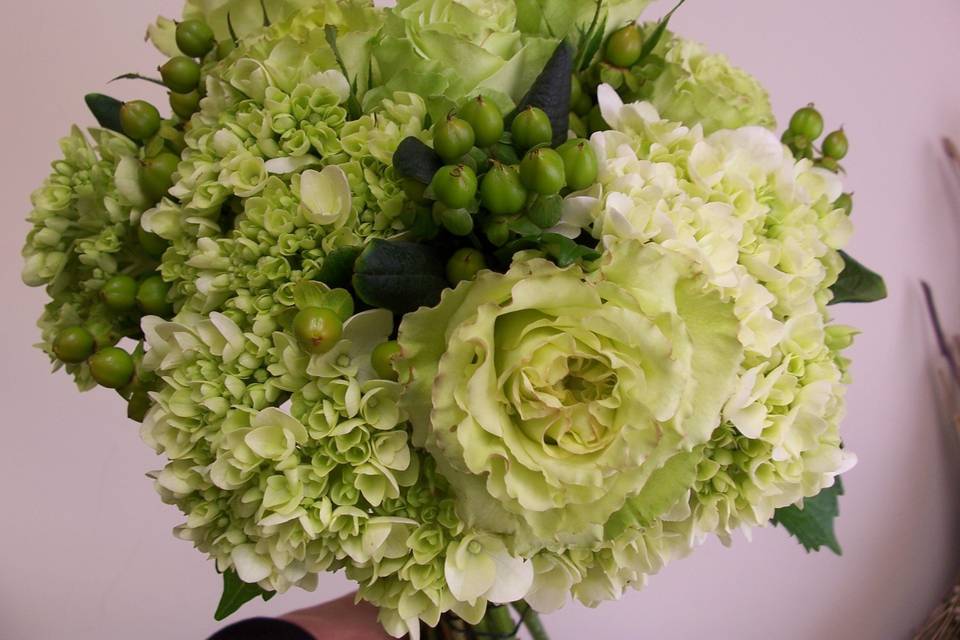 Green hydrangeas, roses and hypericum in a hand tied bouquet.