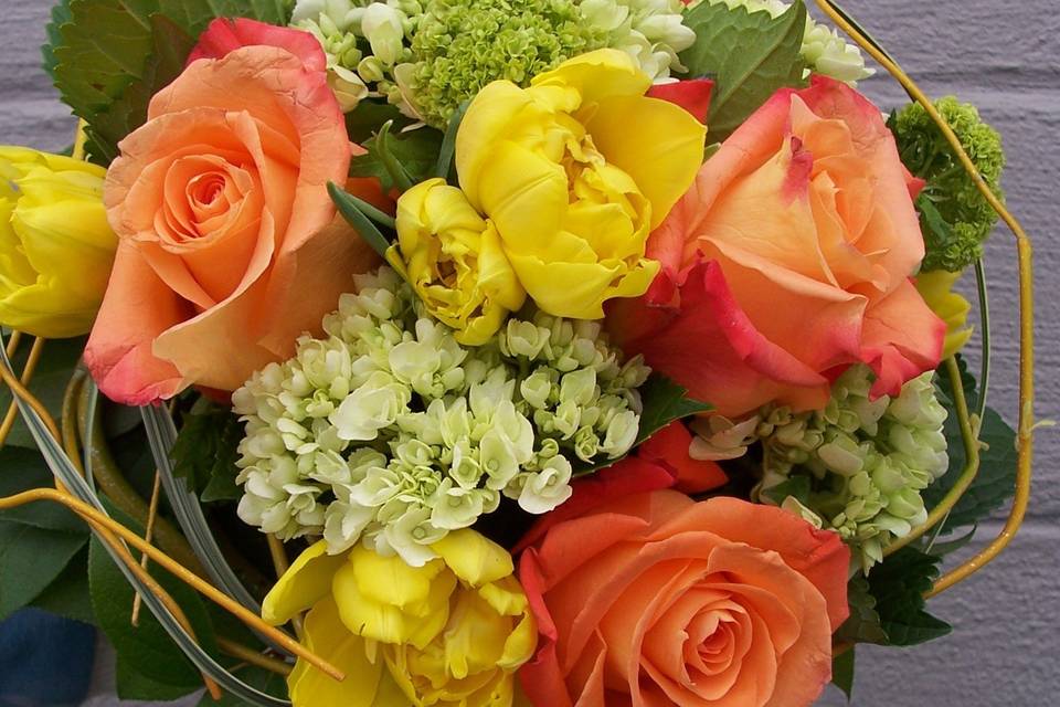 Happy spring colors of orange roses, yellow tulips, hydrangeas and a collar of curly willow frame this bouquet.