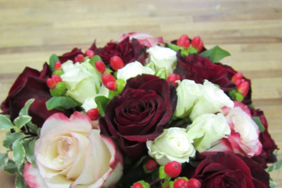 Deep red and bi color roses with white spray roses and red hypericum berries in a hand tied bouquet accented with variegated mini pitt.