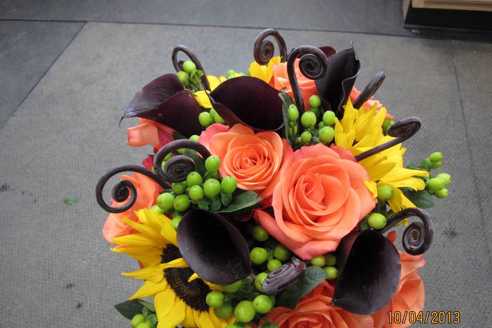 Dark calla lilies, uhle, roses, hypericum and sunflowers in a hand held bouquet.
