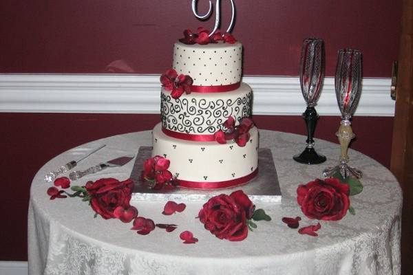 3 tier round buttercream wedding cake with black sroll work, swiss dots, red ribbon, and red roses.