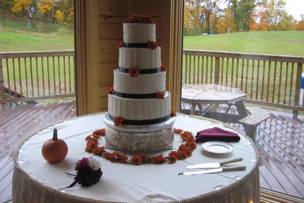 4 tier round buttercream cake with swiss dots, vertical stripes and chocolate brown ribbon.