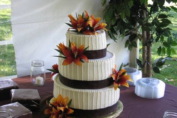 3 tier round buttercream cake with vertical stripes and brown ribbon.