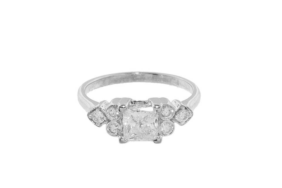 This gorgeous ring from Sethi Couture is host to a stunning princess cut center diamond that has a carat weight of .70 carats. It is detailed with a triplet of bezel set diamonds on either side, creating a total carat weight of .89 carats. It is finished in 18 karat white gold and would make a stunning engagement ring.