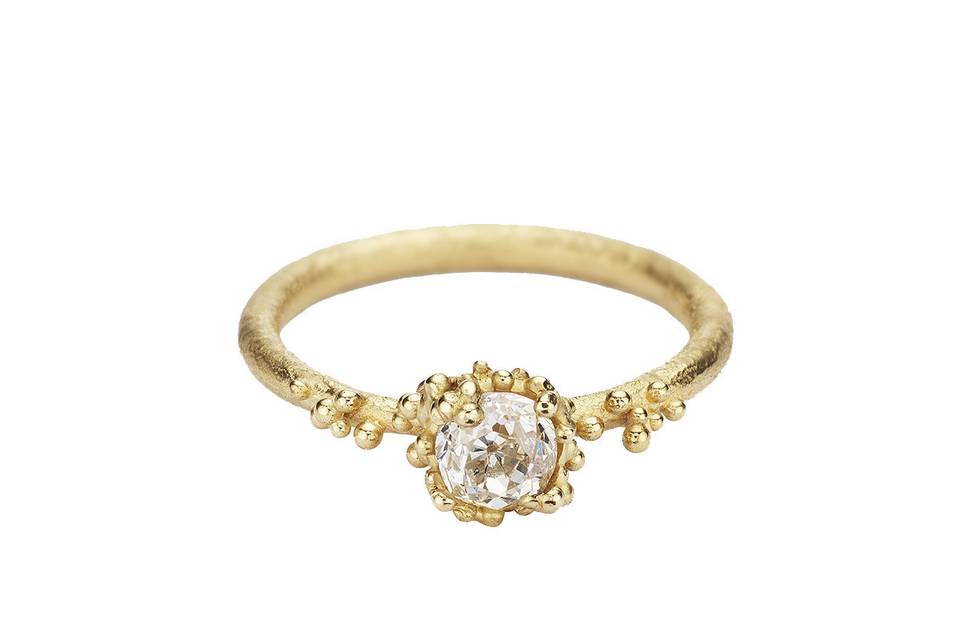 Detailed by hand this Ruth Tomlinson ring glistens from a .05 carat antique cut white diamond. This diamond rests in granules of 18 karat yellow gold on a lightly textured band.