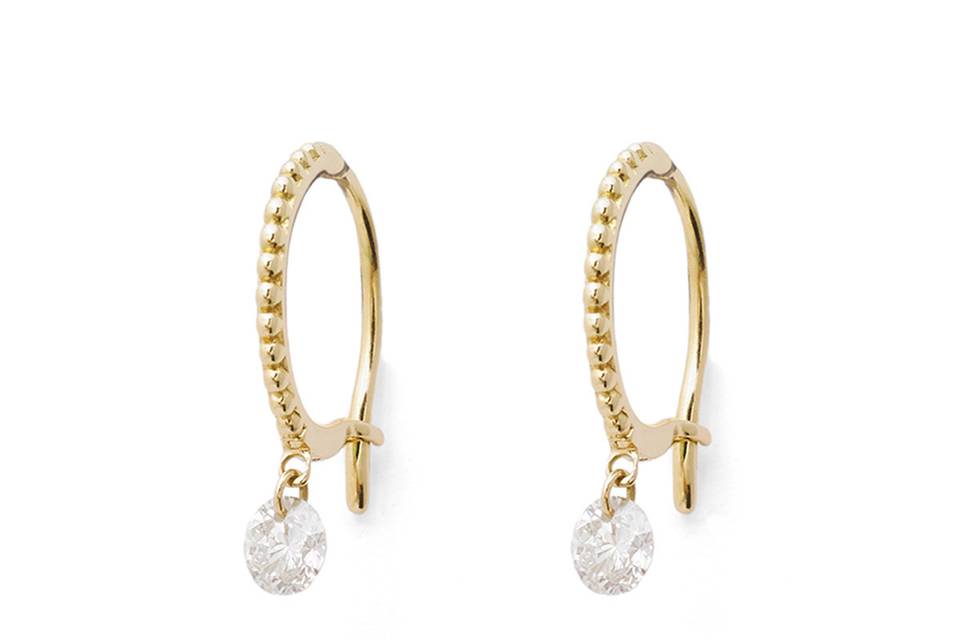 These staple hoop earrings from Raphaele Canot are a great everyday piece. These hoops are set in 18 karat yellow gold and feature a beaded motif that adds a vintage edge. Accented with a large white diamond that dangles freely from the hoops. The diamonds total .20 carats. Measure 3/8
