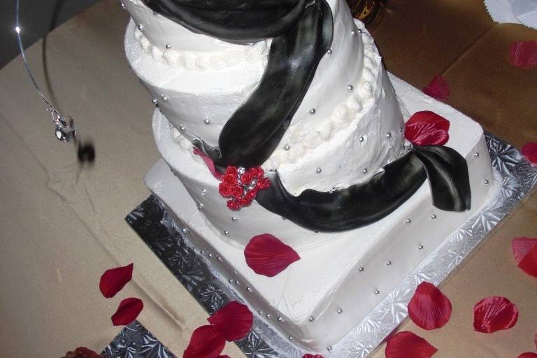 Buttercream covered cake with black fondant swag, red silk flowers and decorative cake jewelry provided by the bride.