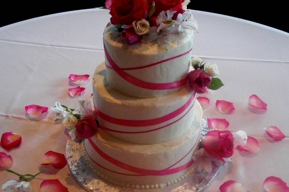 Buttercream covered cake with simple fuchsia ribbon and fresh flowers for decoration.