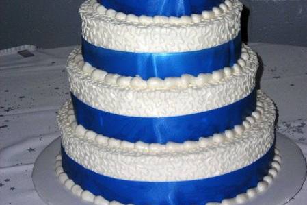 Stacked wedding cake with white buttercream icing adorned with blue satin ribbon and a floral cake topper.