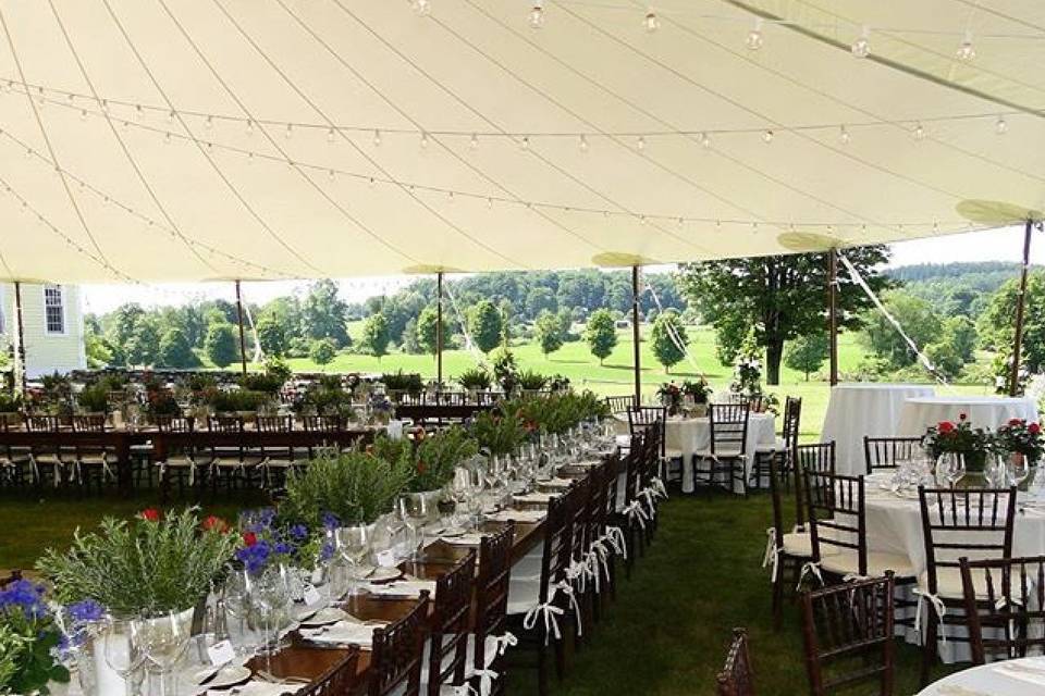 Inside Stillwater sail cloth tent with farm tables and fruitwood chivari chairs