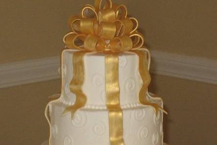 Round, stacked tiers, iced in buttercream accented with edible gold bow and streaming ribbons.