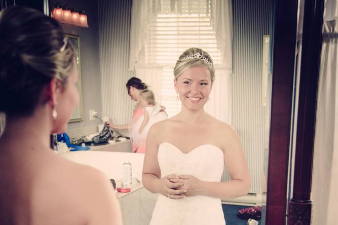 Bride in Mirror. Flower girl and mom getting ready in the background.