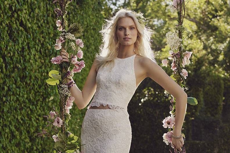 Casablanca Bridal Style 2241 - Heather <br> Heather is a fashion forward two-piece dress is anything but traditional, yet its modern sheath silhouette and fashion forward halter top remain uniquely bridal. Tasteful, non-beaded floral lace blossom over the halter top with its open back, as well as the skirt.