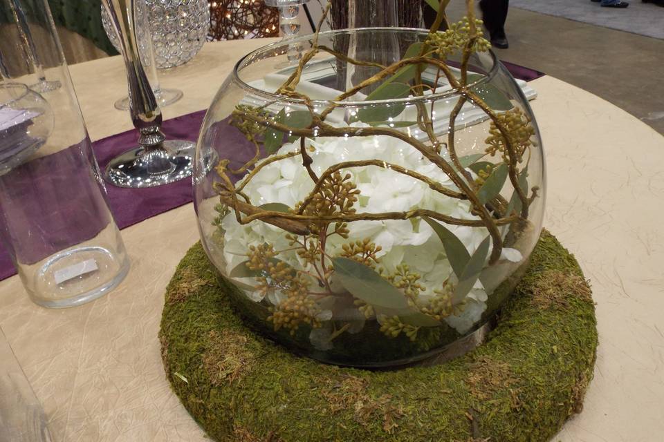 A beautiful natural inspired centerpiece that rests in a moss covered ring.  Inside, submerged white hydrangeas with caging of curly willow accented in seeded eucalyptus.  It's a great choice for a lower budget and natural look.