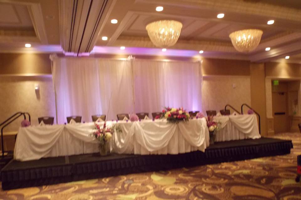 This beautiful back drop and head table at the Crowne Plaza of Lansing.  The subtle lighting and bunted linen front accented in floral is a perfect focal point.