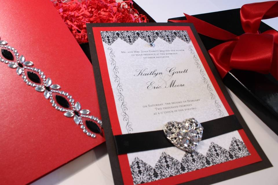 Custom Musical Wedding Invitations - the Brocade Romance can be customized in your choice of colors - shown here in red and black, it has a keepsake heart brooch on the satin ribbon. The holder has elegant black and crystal embellishment and the black box features a red satin ribbon. Best of all, romantic music plays when the box opens and closes. Comes with RSVP card and envelope. See other picture views.