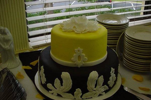 Wedding cake: Two tier covered in black and yellow fondant, accented with flowers, leaves and ribbon. Reception held at Oceanside Inn and Suites on Jekyll Island, Georgia.