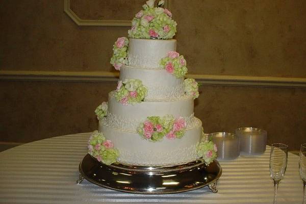 Four tier buttercream with bands of lace accented with flower arrangements, held at First Baptist Church, Brunswick, Ga.